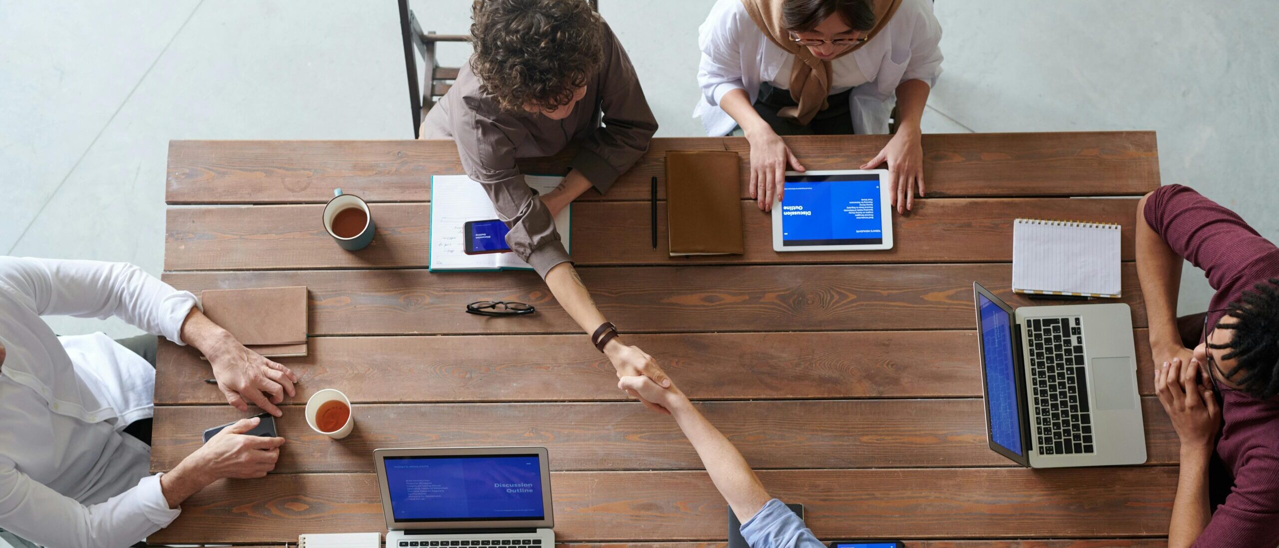 Overhead view of colleagues in a work meeting using laptops and tablets, emphasizing teamwork and technology.